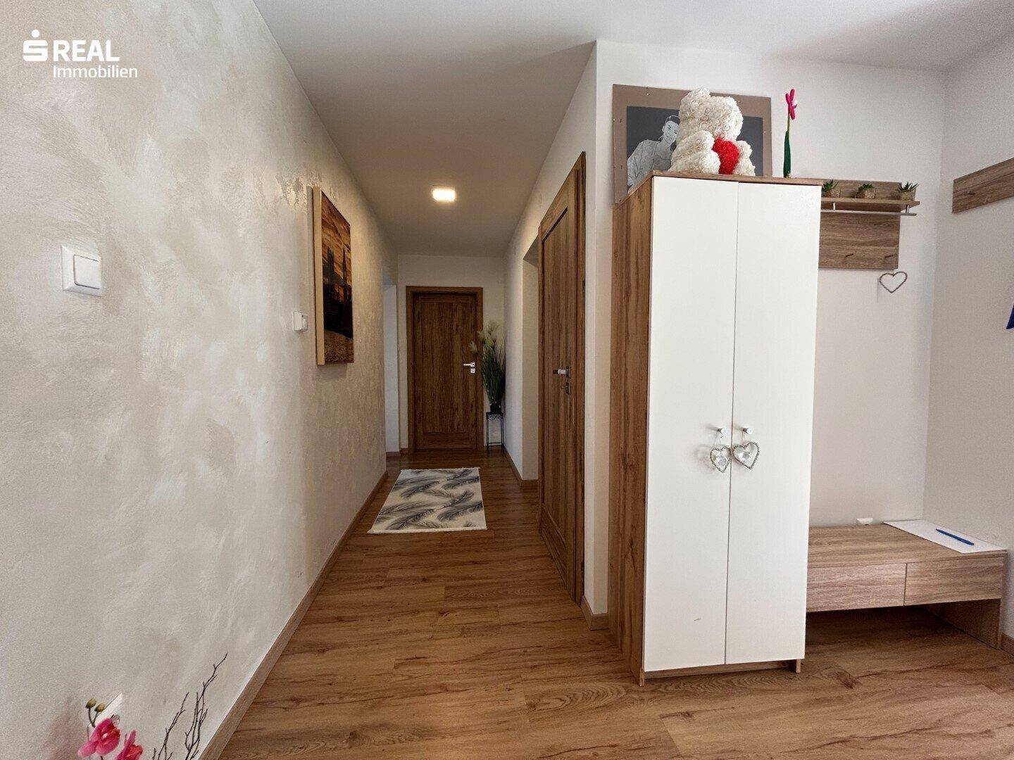 Heller Flur mit Holzboden, weiß gestrichenen Wänden und praktischer Garderobe.