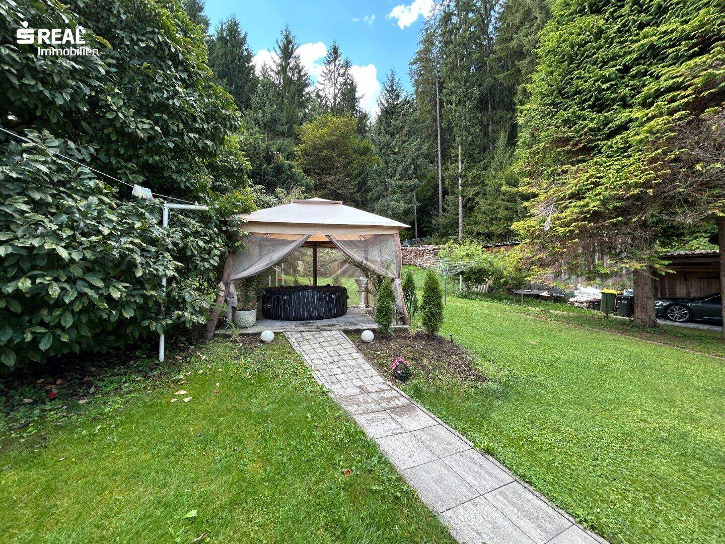 Gepflegter Gartenbereich mit gepflastertem Weg, Pavillon und Whirlpool umgeben von Bäumen.