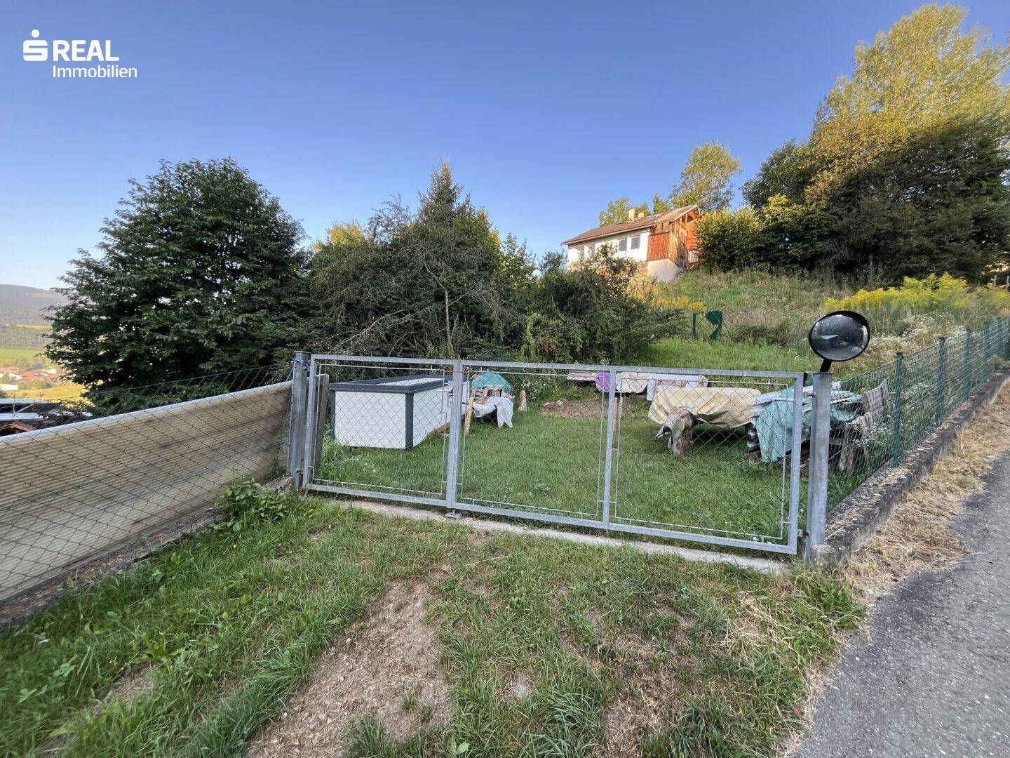 Eingangsbereich zum Garten mit Metallzaun und Blick auf das umliegende Grün.