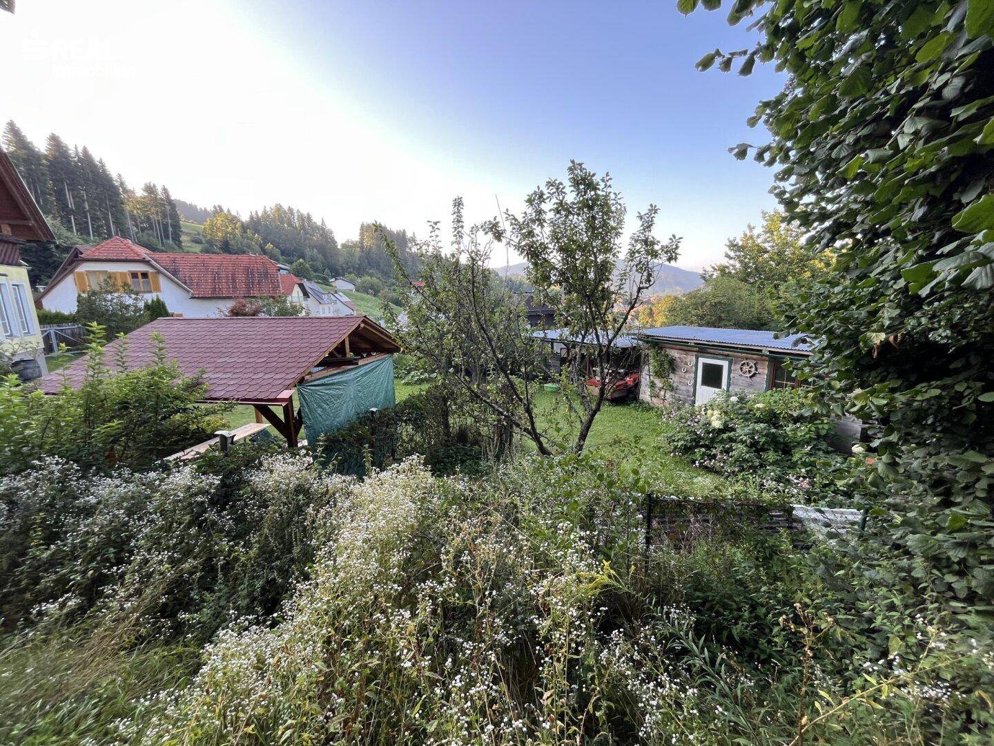Weitläufiger Gartenbereich mit Bäumen, Sträuchern und Blick auf die umliegende Landschaft.