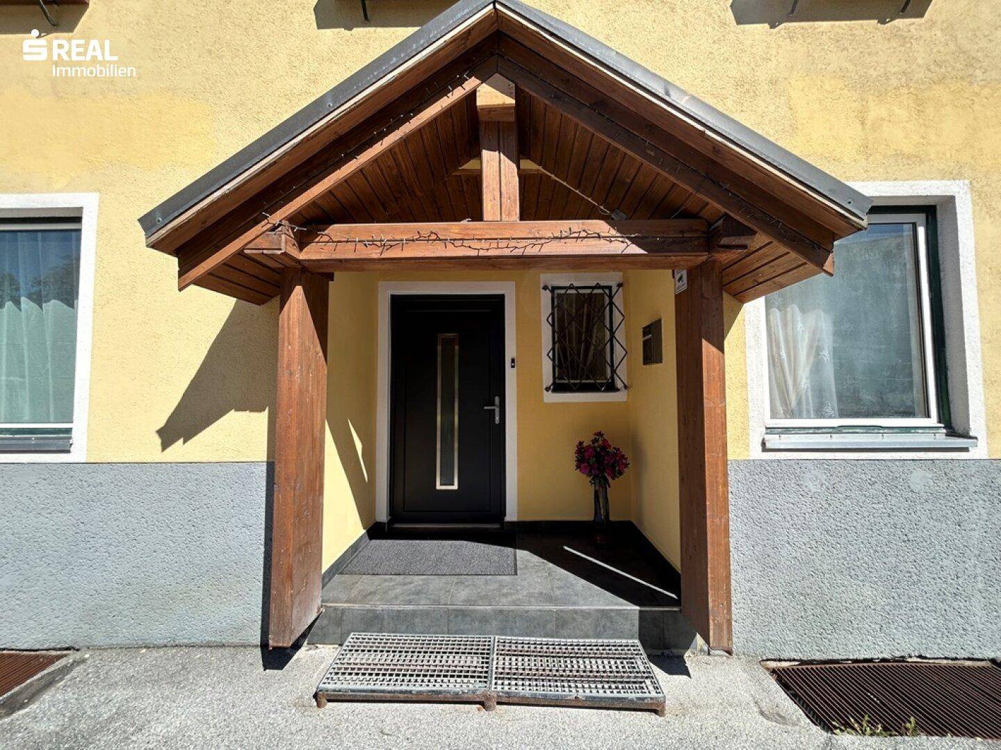 Eingangsbereich des Gebäudes mit Holzvordach und dunkler Eingangstür.