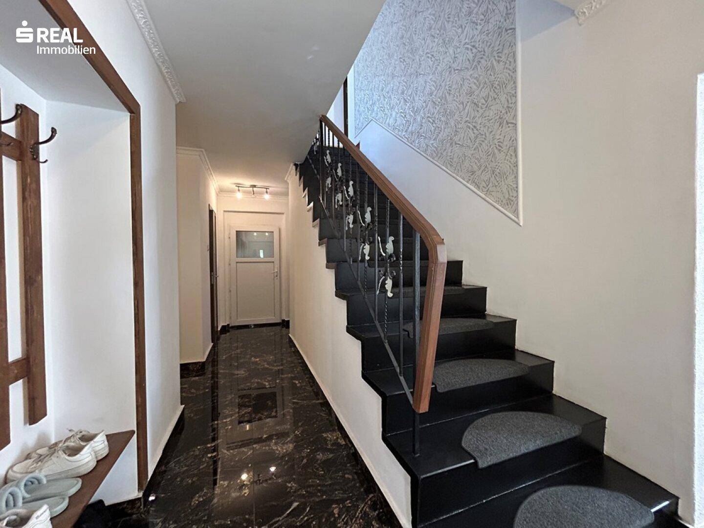 Geräumiger Flur mit dunklem Fliesenboden und Treppe mit schmiedeeisernem Geländer.