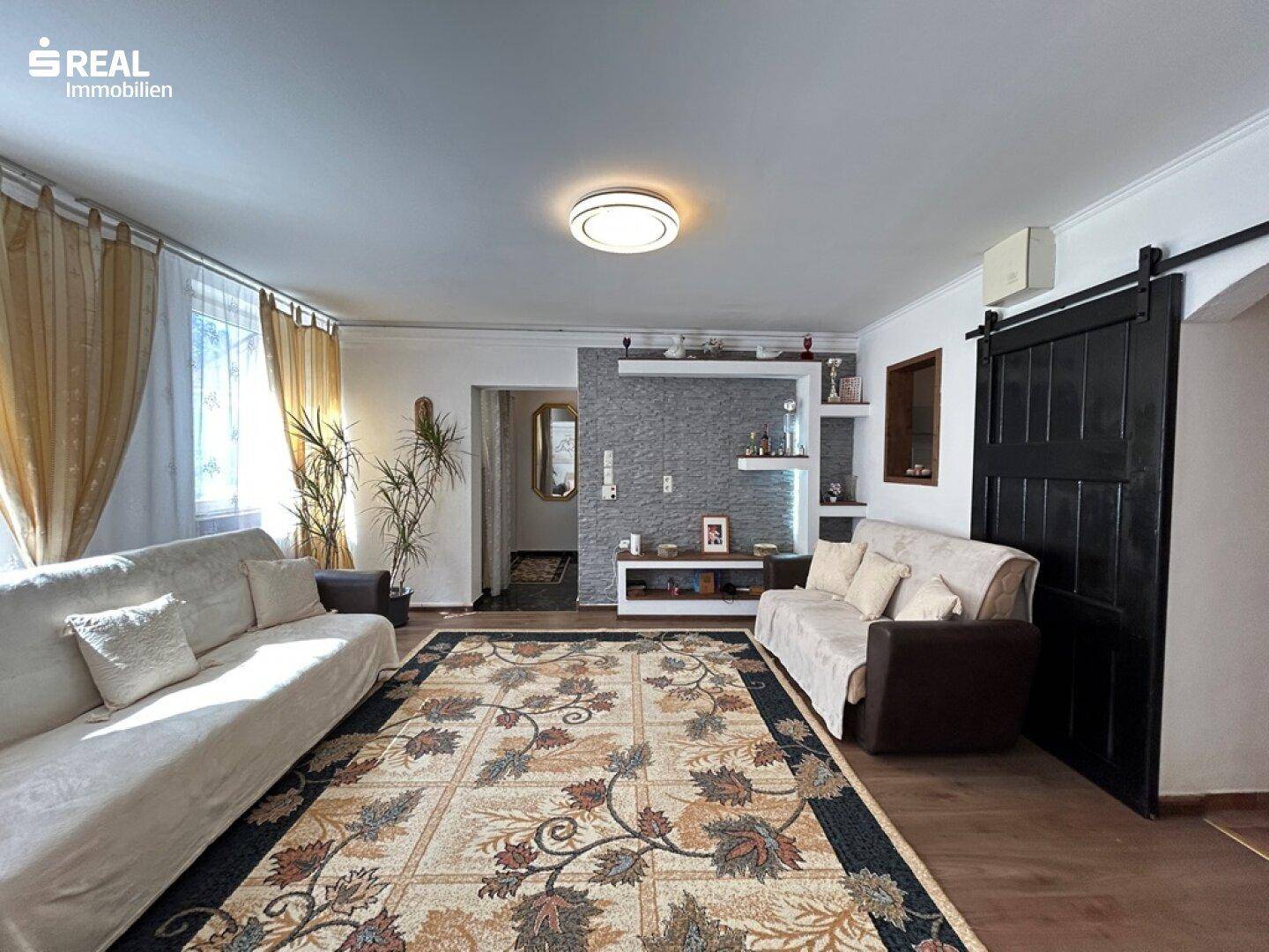 Helles Wohnzimmer mit zwei Sofas, Holzboden und dekorativer Wandgestaltung.
