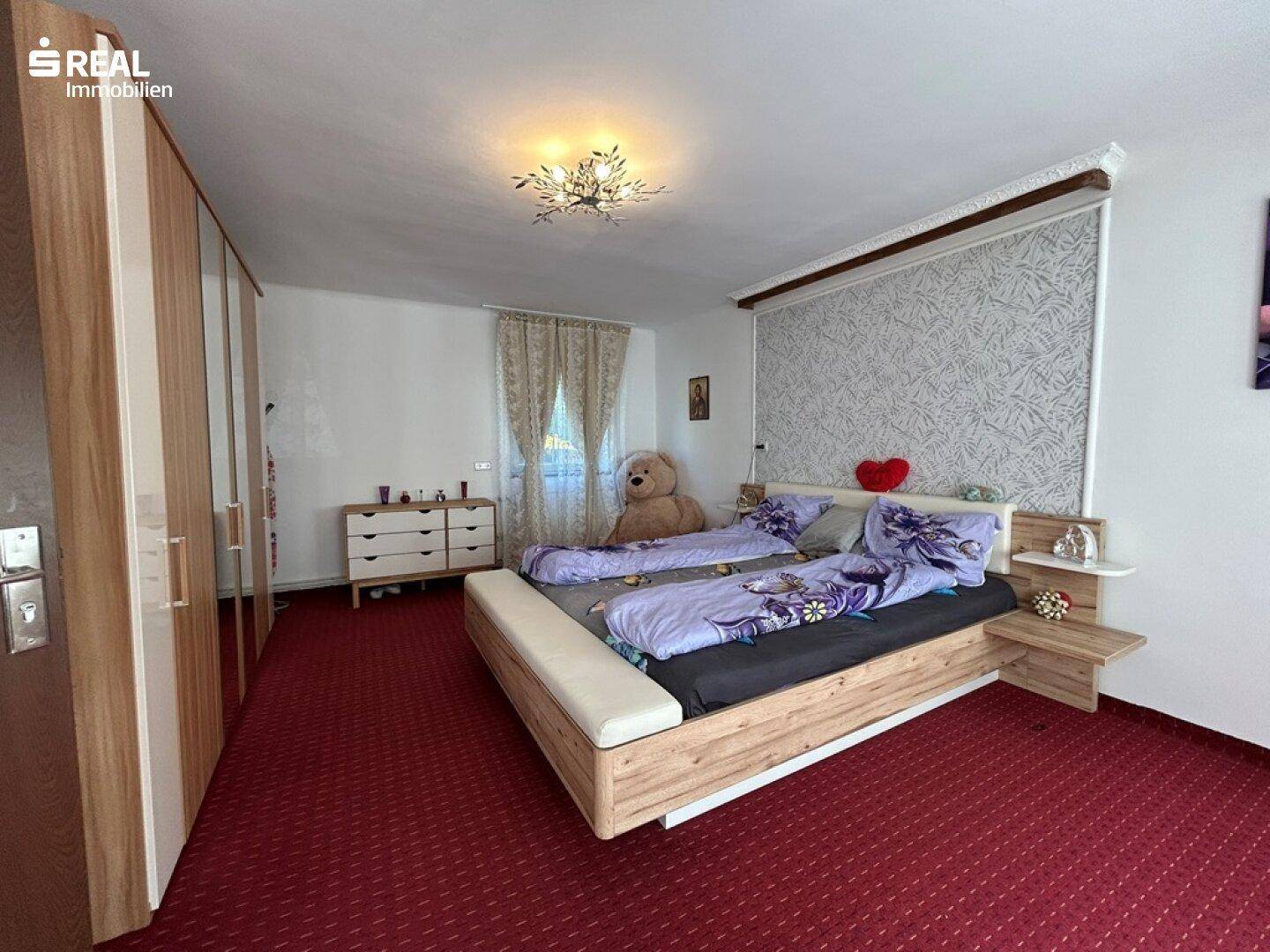 Schlafzimmer mit Doppelbett, rotem Teppichboden und Spiegelschränken.