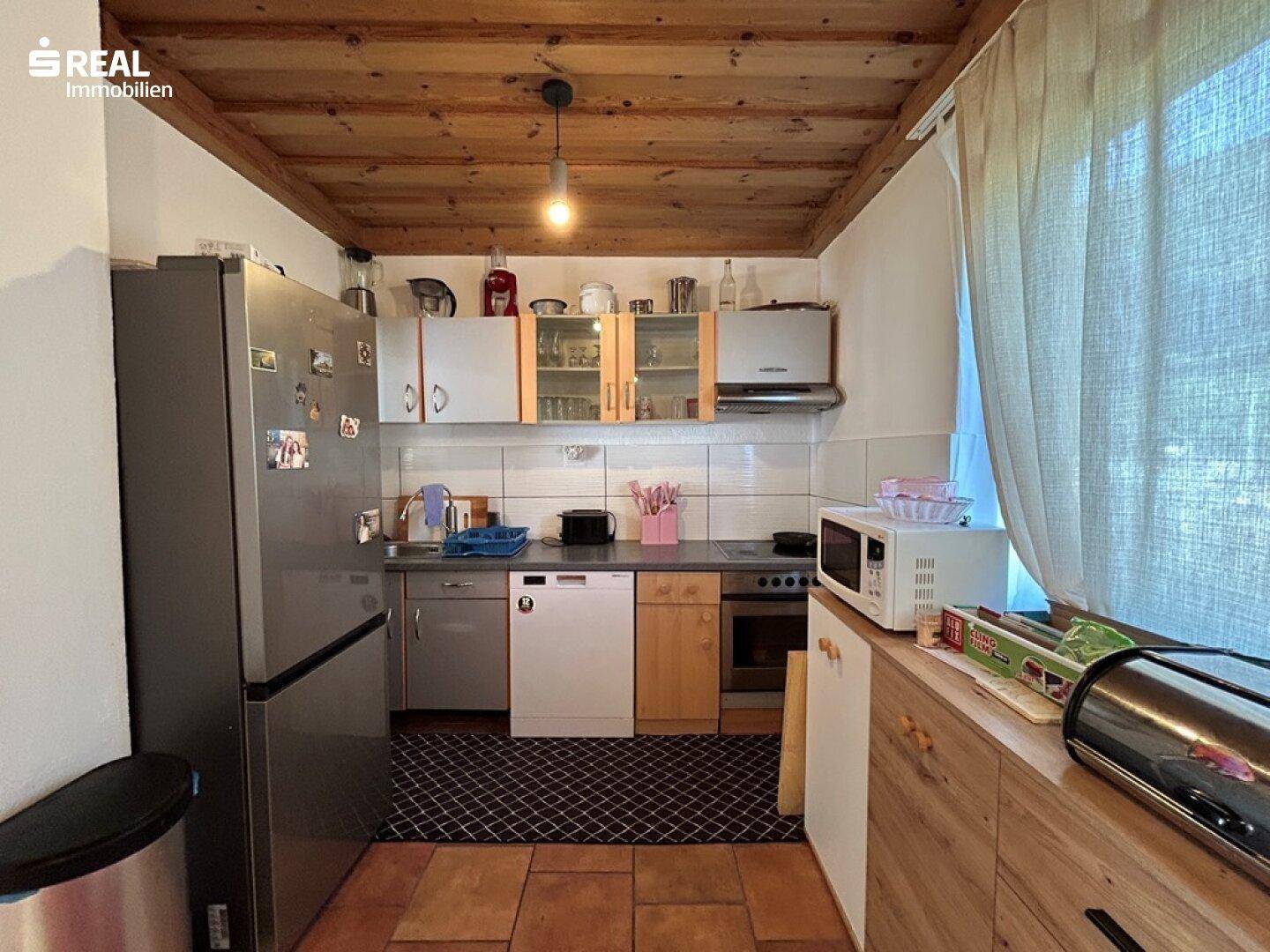 Funktionale Küche mit Holzdecke, Terrakottafliesen und Einbaugeräten.