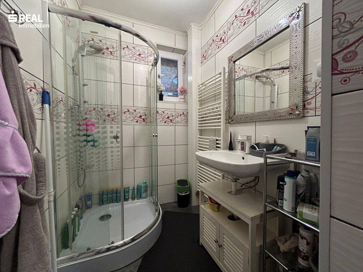 Badezimmer mit Duschkabine, Waschbecken und beheiztem Handtuchhalter.
