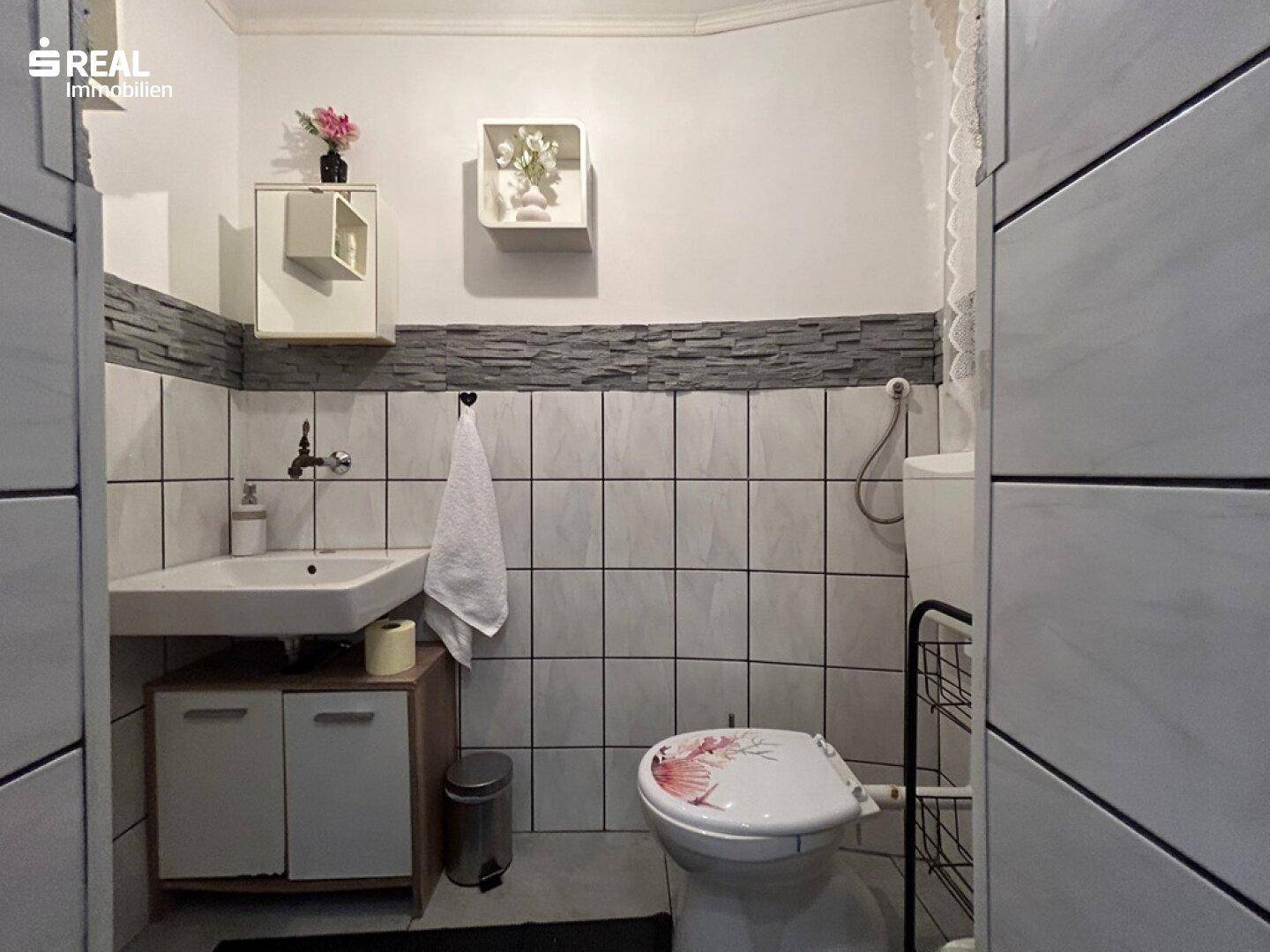Gäste-WC mit Waschbecken, Toilette und Wandfliesen in Steinoptik.