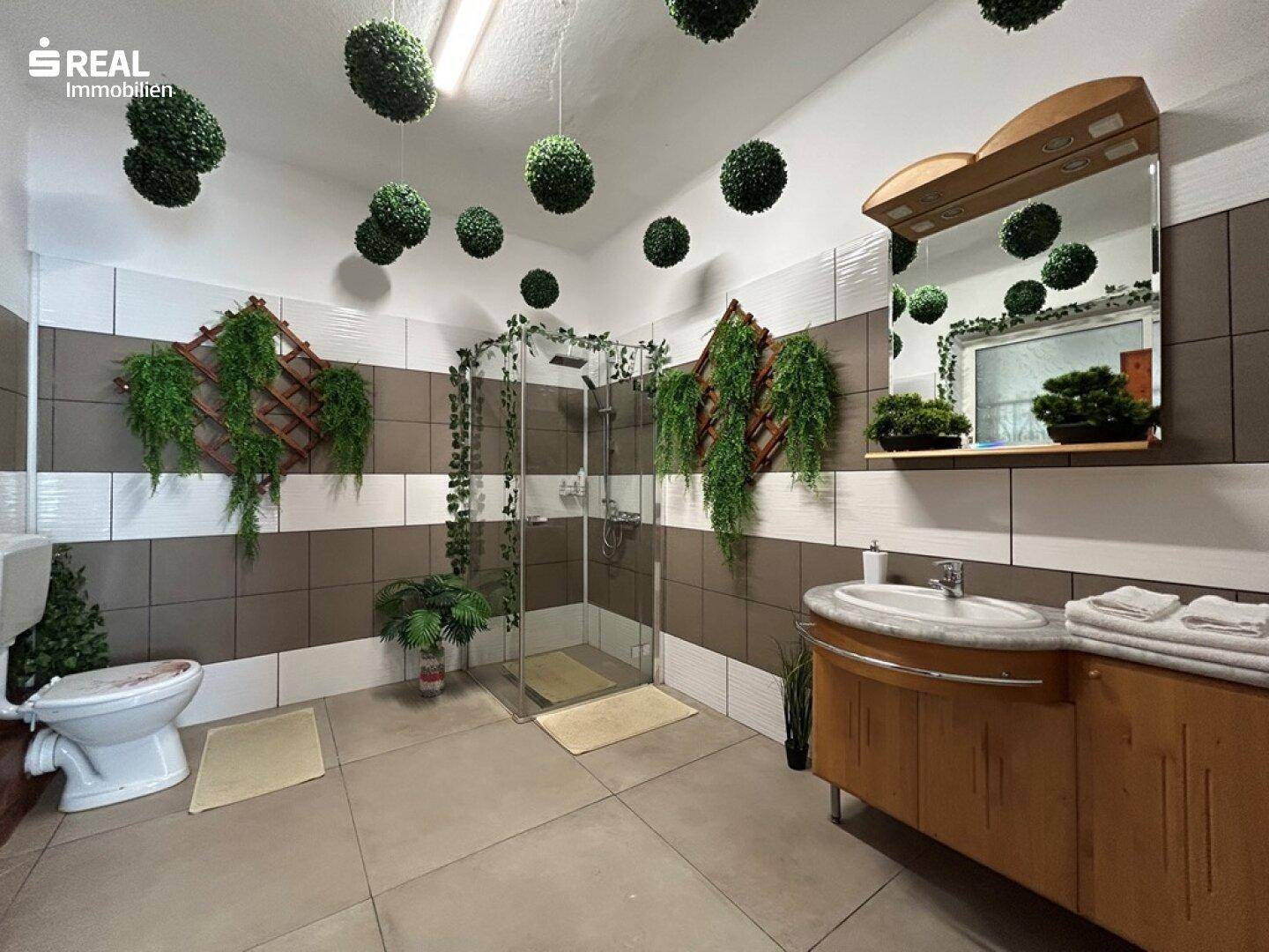 Modernes Badezimmer mit Duschkabine, Waschbecken und dekorativen Pflanzen.