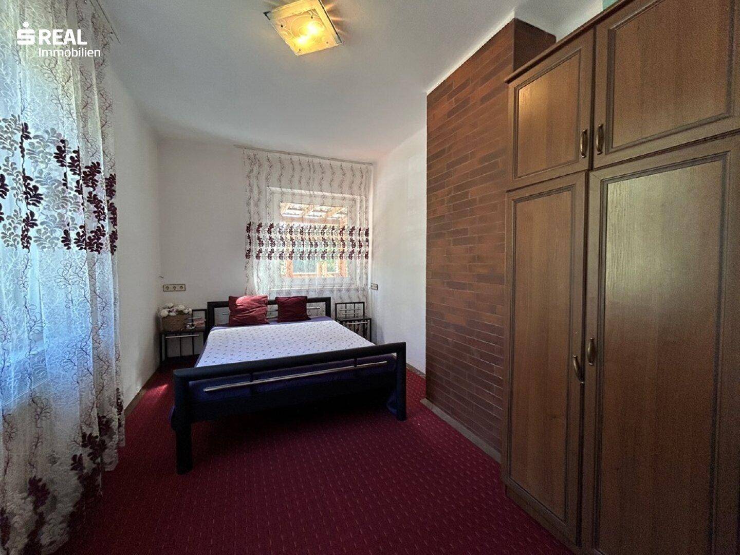 Schlafzimmer mit Doppelbett, rotem Teppichboden und Holzschrank.