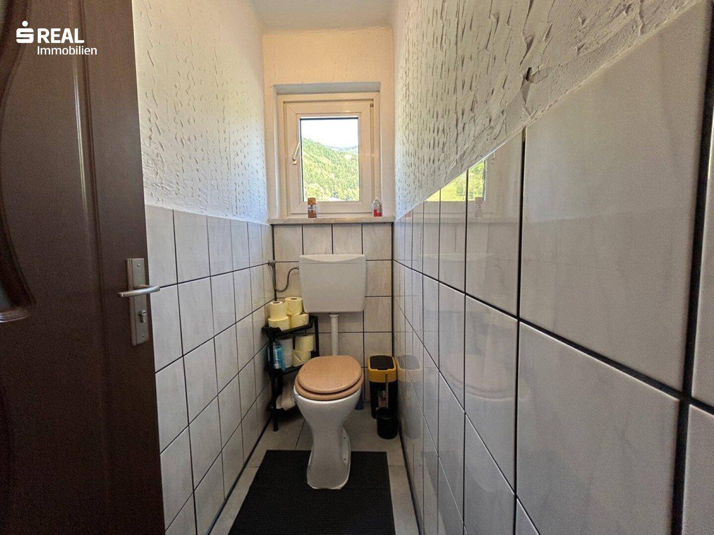 Kleine Gästetoilette mit Fenster und schlichten Fliesen, funktional und hell.
