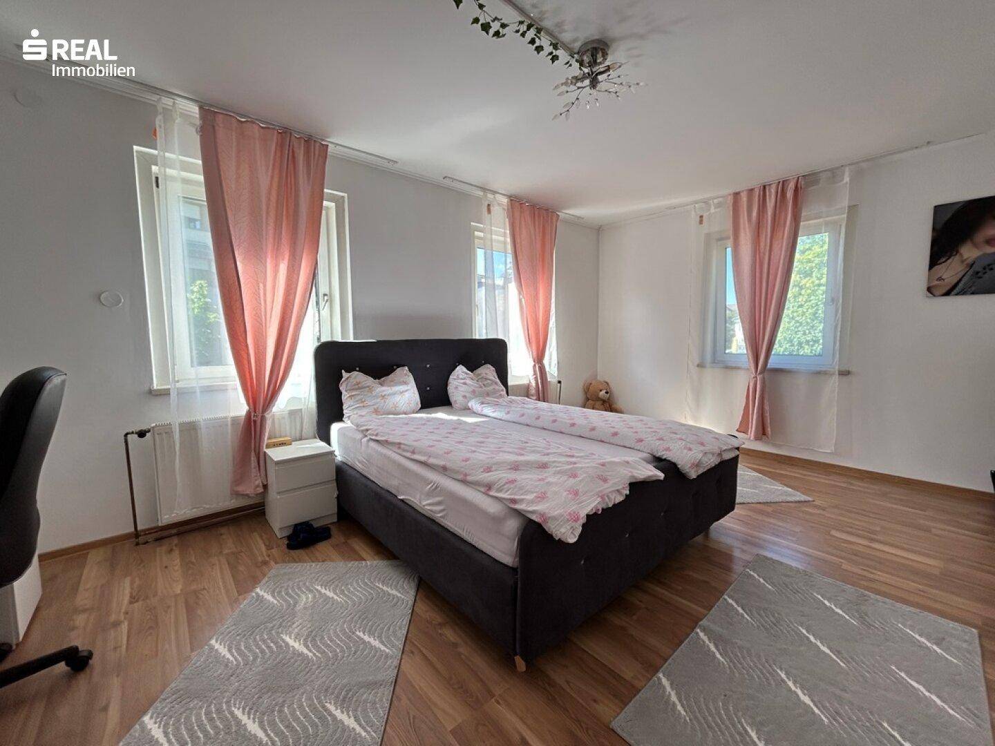 Helles Schlafzimmer mit Doppelbett, Holzfußboden und großen Fenstern.