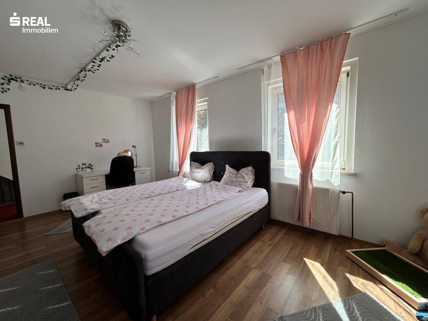 Schlafzimmer mit Doppelbett, Holzfußboden und Schreibtischbereich.