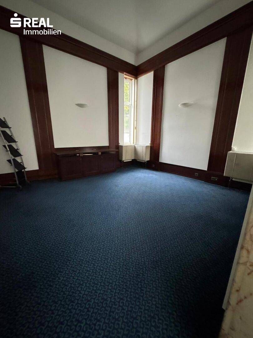 Büroraum mit blauer Teppichboden, weißen Wänden und dunklen Holzvertäfelungen.