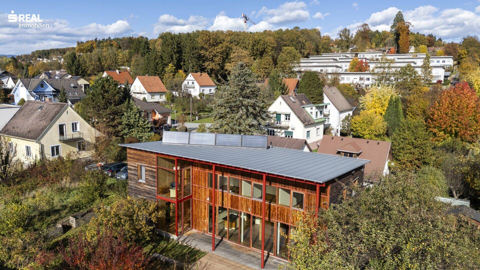 Luftaufnahme des modernen Holzhauses mit Flachdach und der umliegenden grünen Wohngegend.