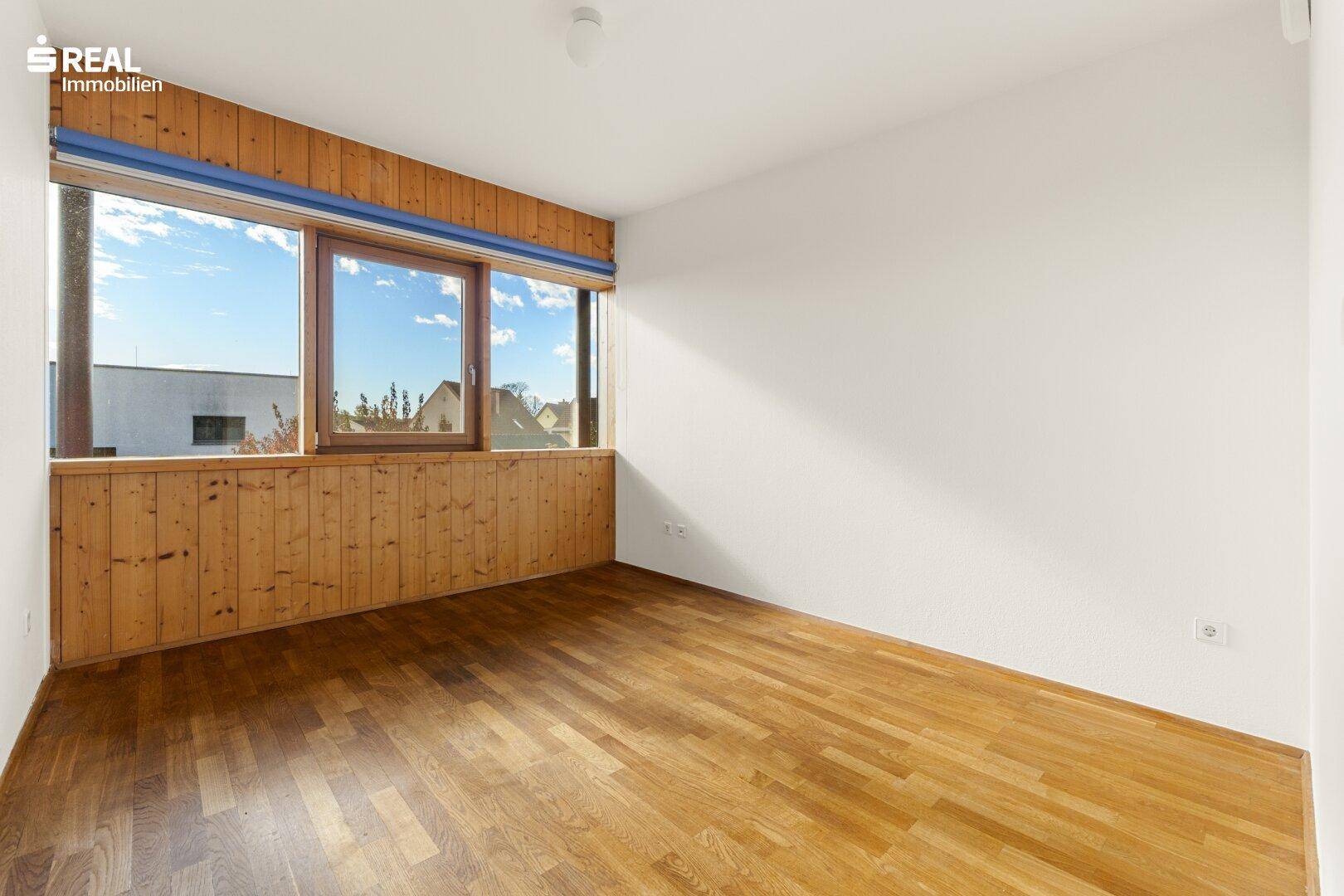 Helles Schlafzimmer mit Holzboden und breiten Fenstern, die einen weiten Ausblick bieten.