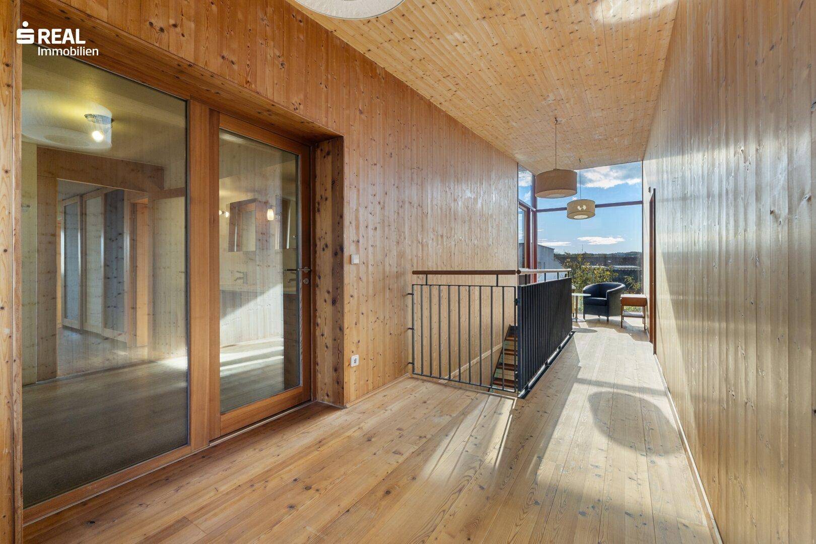 Heller Flur im Obergeschoss mit Holzverkleidung, großen Fenstern und Blick ins Grüne.