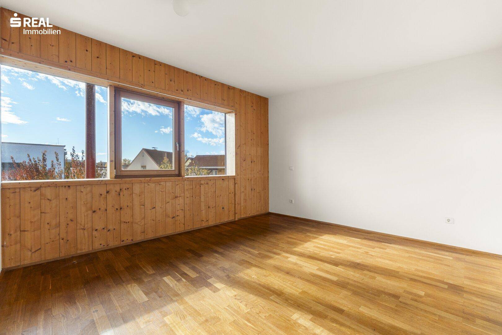 Geräumiges, leeres Schlafzimmer mit Holzboden und breiten Fenstern, die viel Licht spenden.