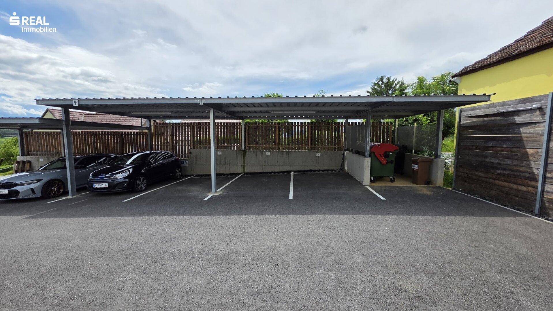 Überdachte Parkplätze (Carports) mit Mülltonnenbereich neben dem Wohngebäude.