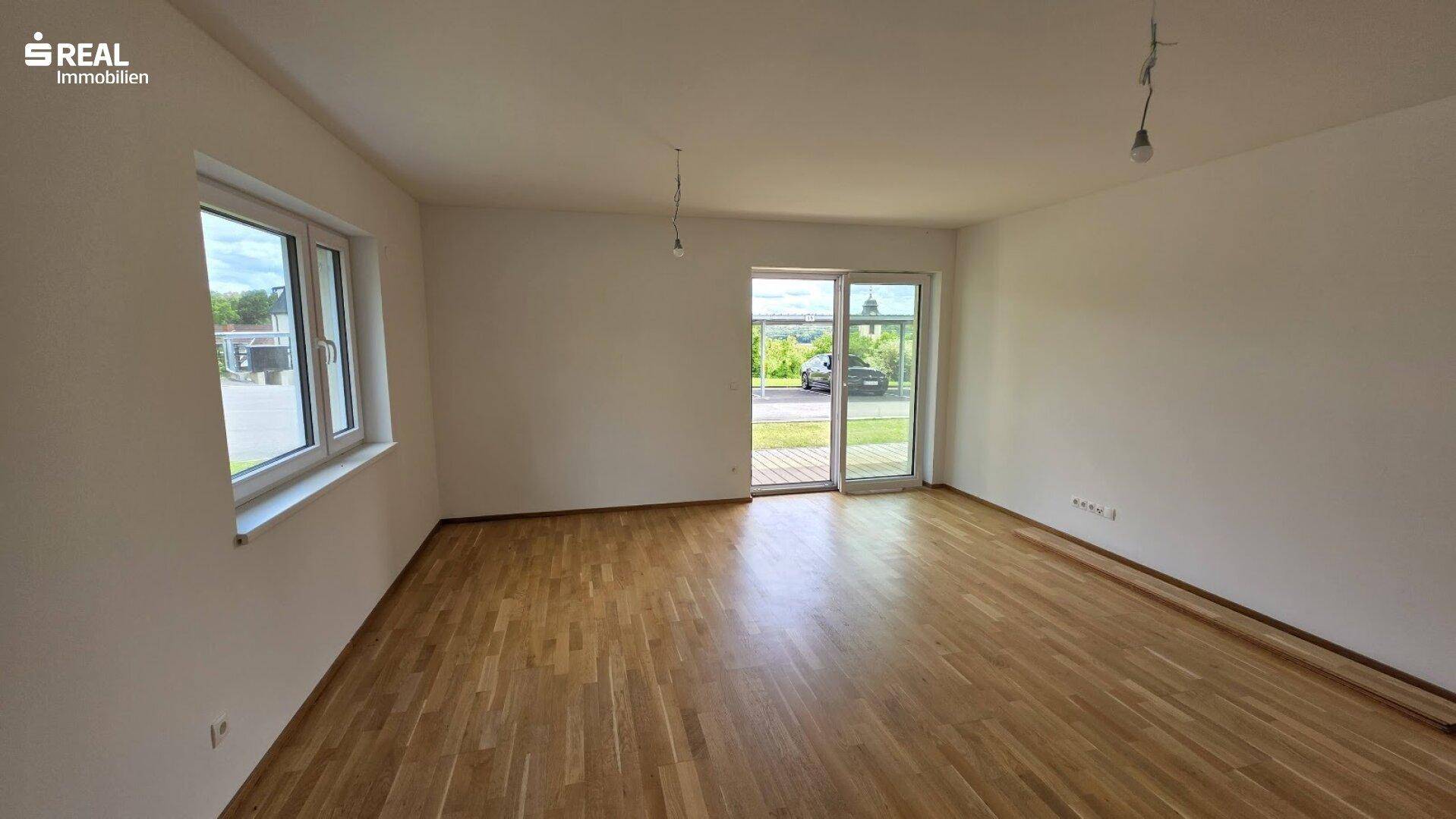 Lichtdurchfluteter Raum mit Parkettboden und Zugang zu einem Außenbereich.