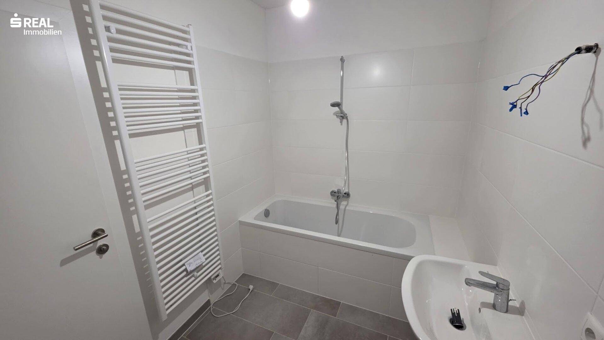 Modernes Badezimmer mit Badewanne, Waschbecken und beheiztem Handtuchhalter.