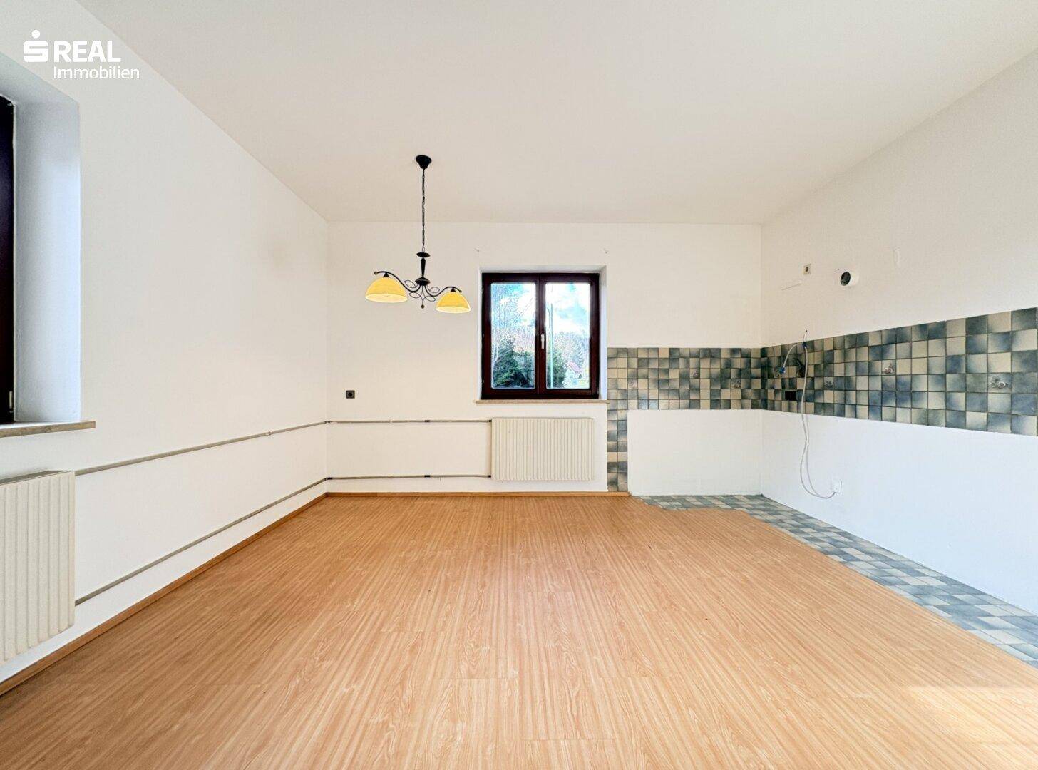 Leere Küche mit Fliesenwand, Fenster und Heizkörper, bereit für neue Einbauten.