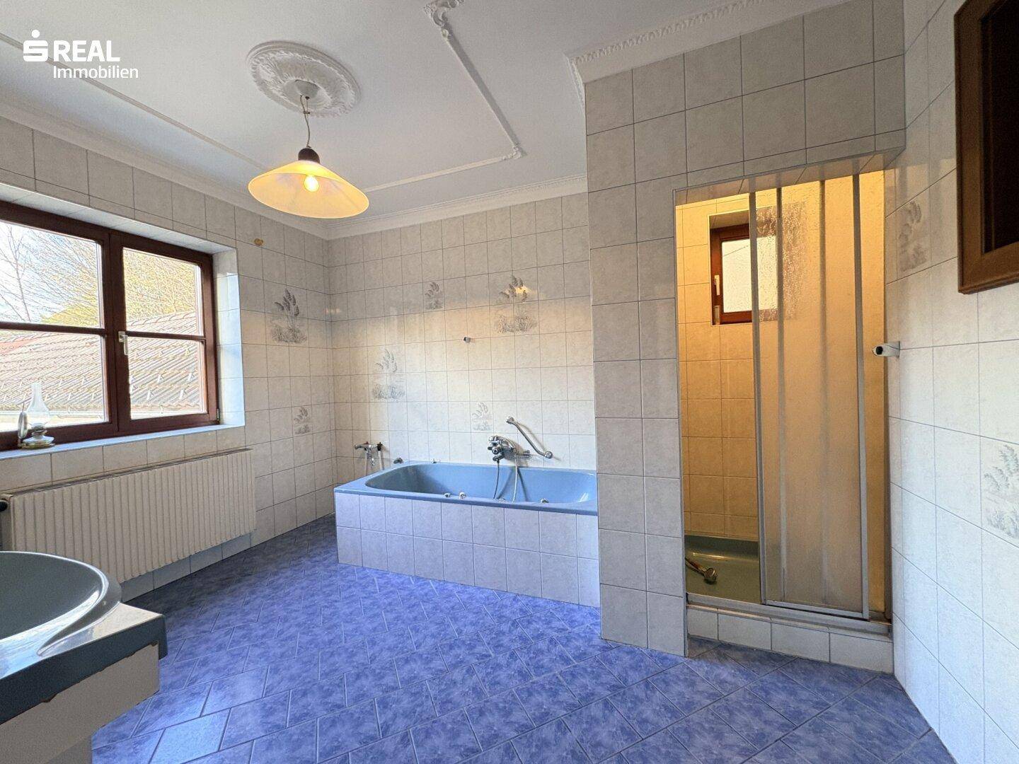 Geräumiges Badezimmer mit blauen Fliesen, Badewanne, Dusche und Fenster.
