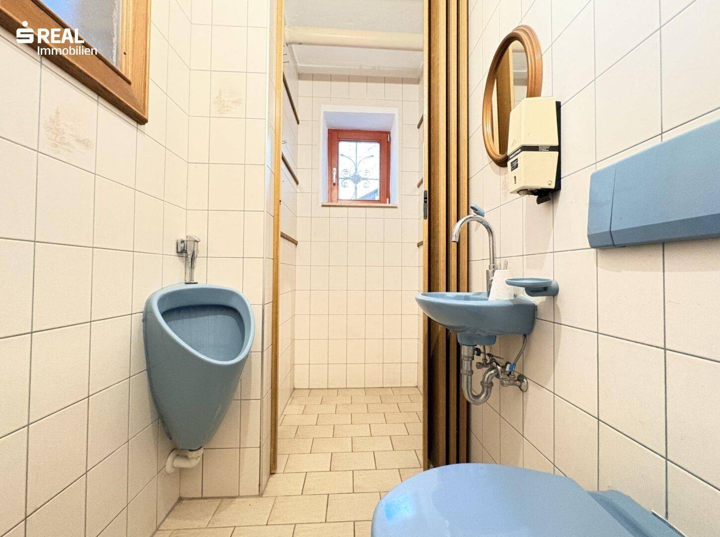 Kleines WC mit blauen Sanitärobjekten, Fliesenwänden und einem Fenster.