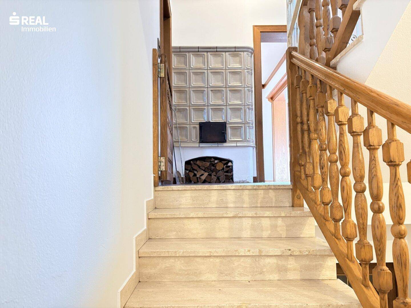 Treppenhaus mit Holzgeländer und Steinstufen, im Hintergrund ein traditioneller Kachelofen.