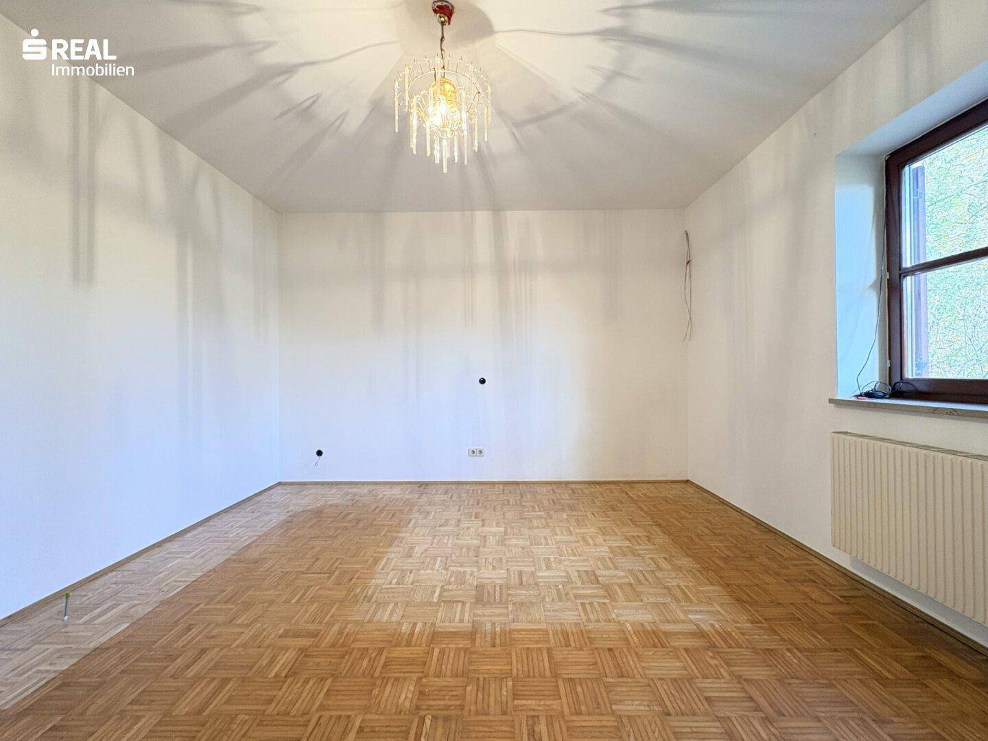 Helles Zimmer mit Fischgrätparkett und großem Fenster, ideal als Schlaf- oder Arbeitszimmer.