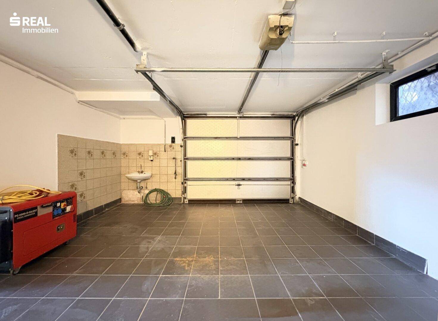 Geräumige Garage mit Fliesenboden, Rolltor und kleinem Fenster.