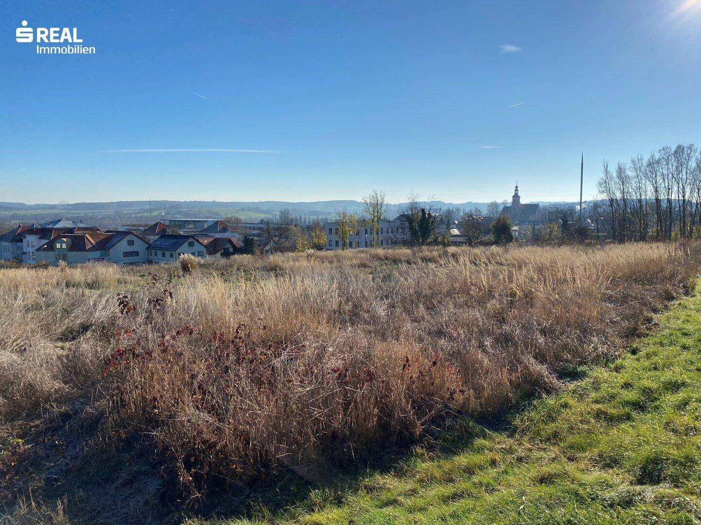 Offenes Feld mit weitem Blick über die Landschaft und eine Siedlung mit Kirchturm im Hintergrund.