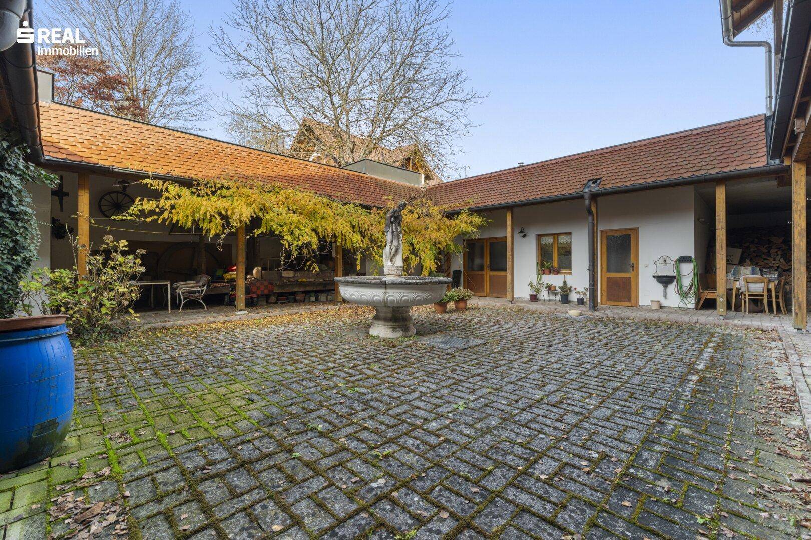 Historischer Innenhof mit Kopfsteinpflaster, einem Brunnen und überdachten Bereichen.