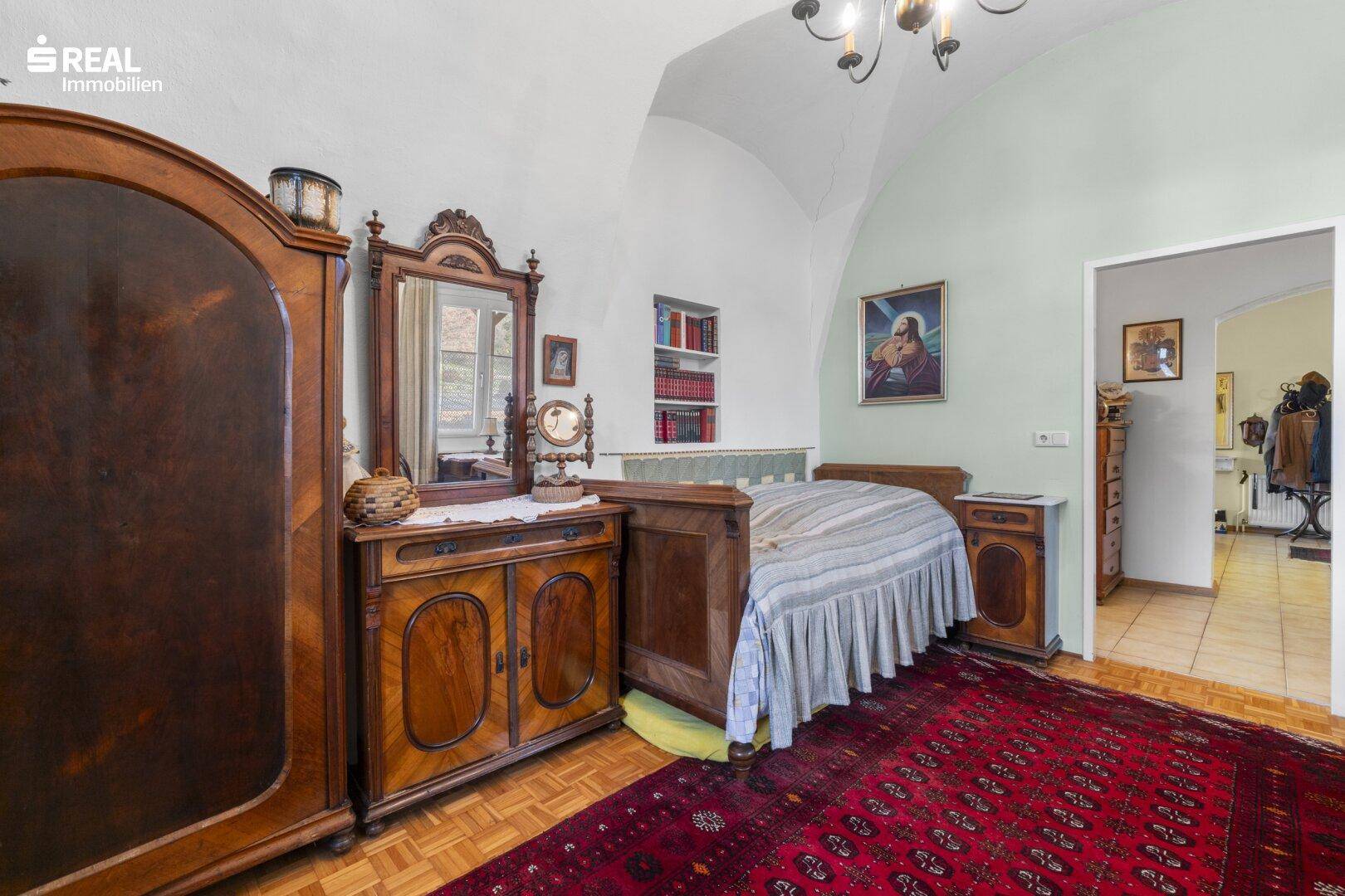 Schlafzimmer mit antiken Holzmöbeln, einem Gewölbe und einem traditionellen Teppich.