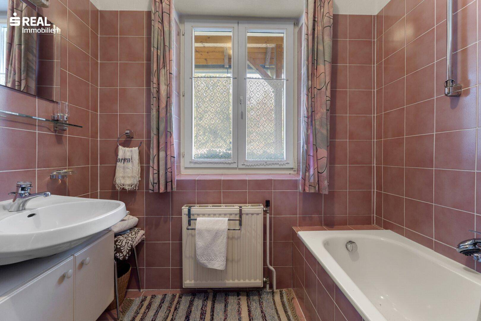 Badezimmer mit rosa Fliesen, Badewanne, Waschbecken und einem Fenster für Tageslicht.