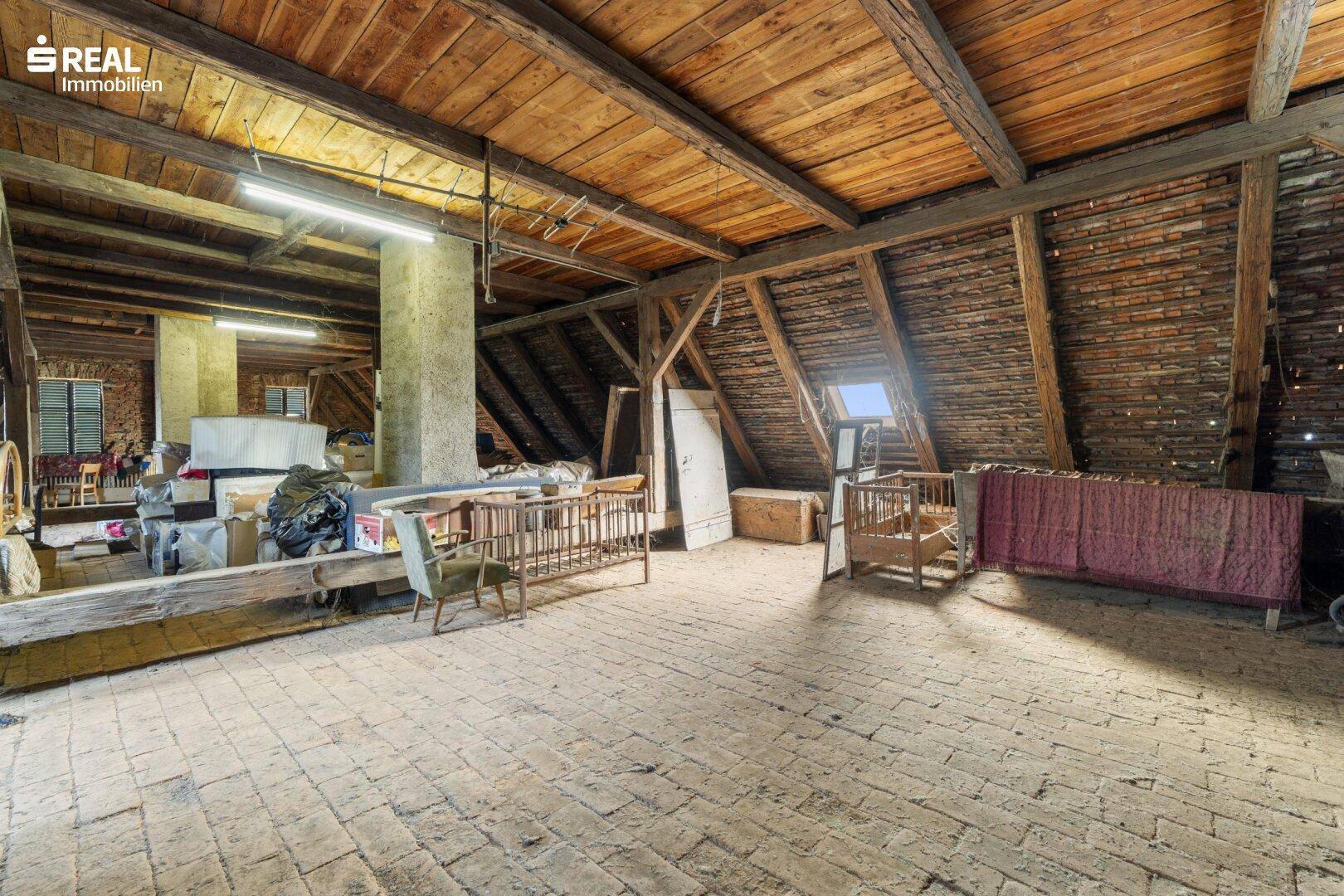 Geräumiger Dachboden mit sichtbaren Holzbalken und Ziegelboden, ideal für Ausbau.