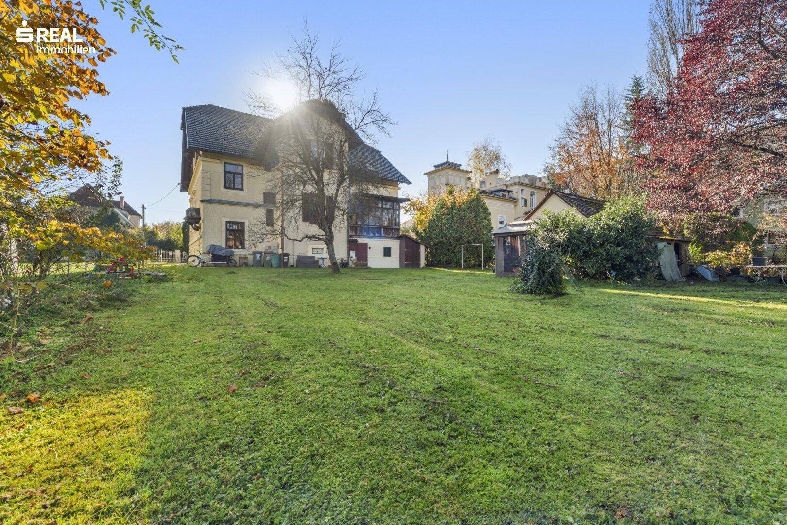 Weitläufiger Gartenbereich hinter der Villa mit großer Rasenfläche und altem Baumbestand.