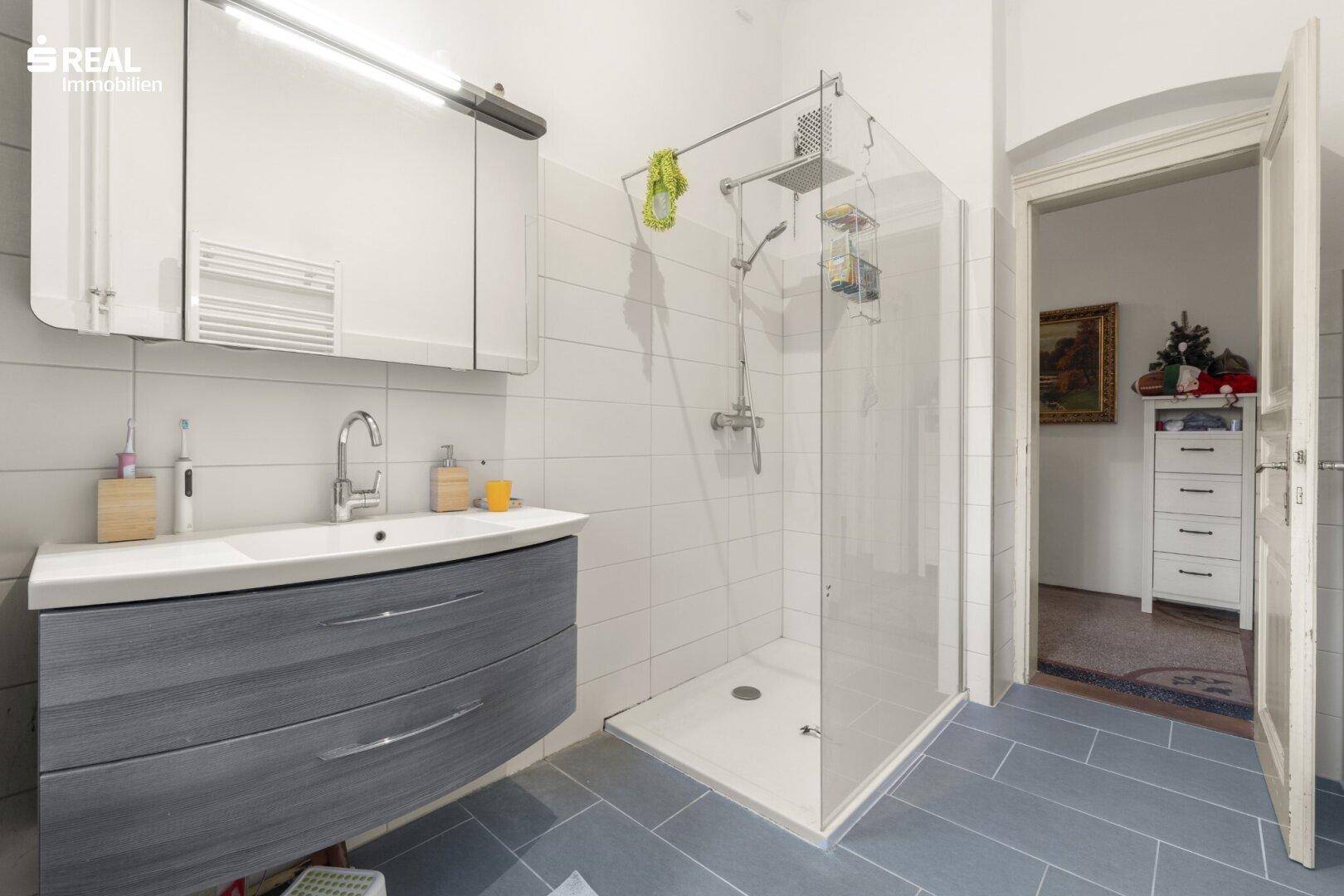 Zeitgemäßes Badezimmer mit großer Dusche, modernem Waschtisch und hellen Fliesen.