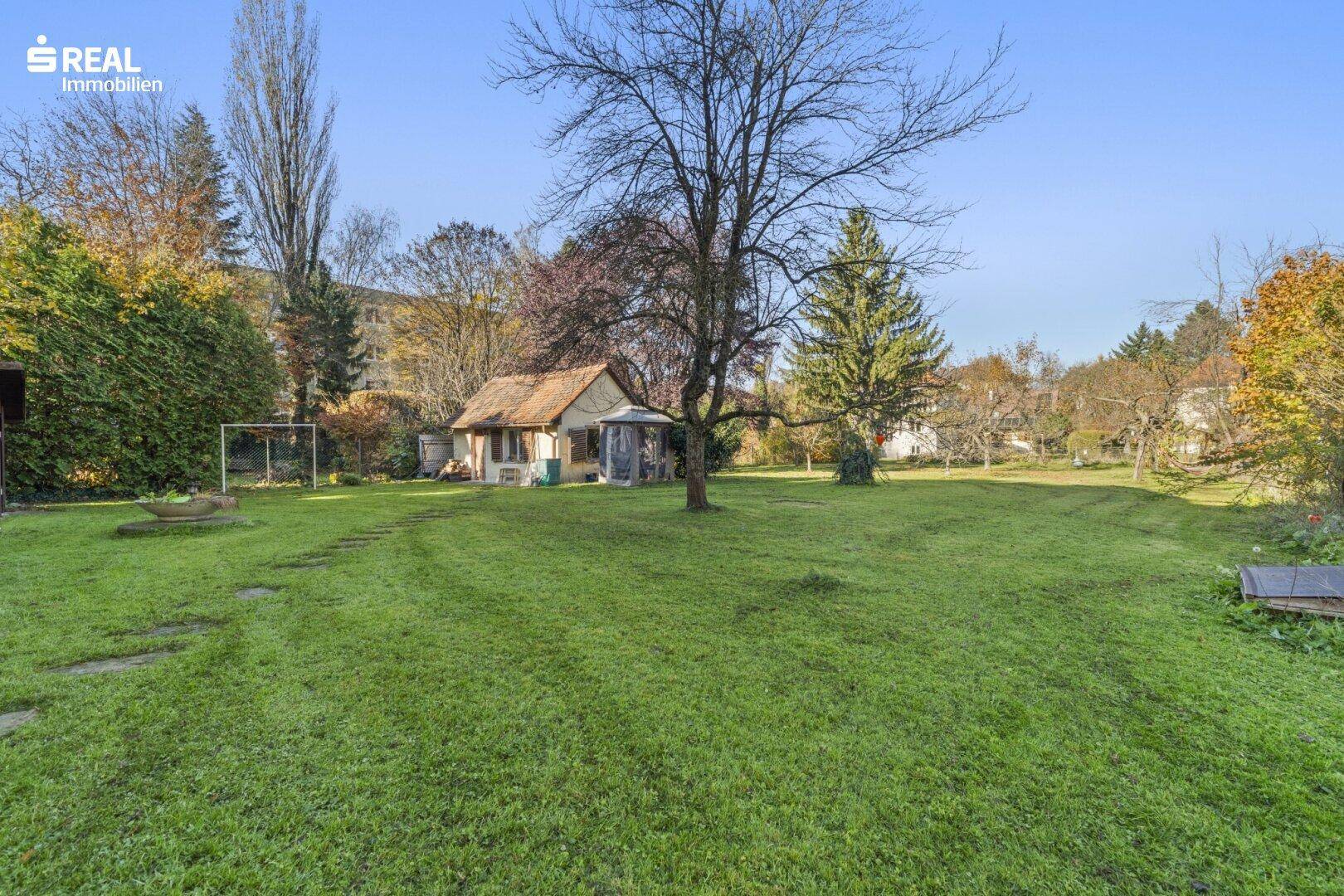 Großer, gepflegter Garten mit Rasenfläche, Bäumen und einem kleinen Gartenhaus.