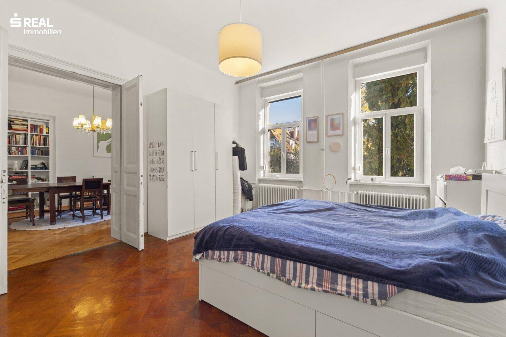 Helles Schlafzimmer mit Parkettboden und Blick ins Grüne, verbunden mit dem Essbereich.