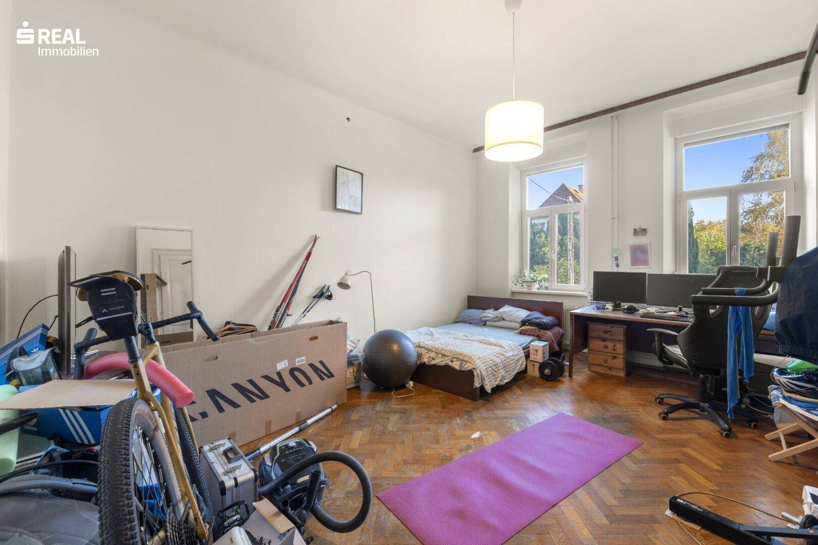 Vielseitiges Zimmer mit Parkettboden, Schreibtisch und Sportgeräten, hell und geräumig.