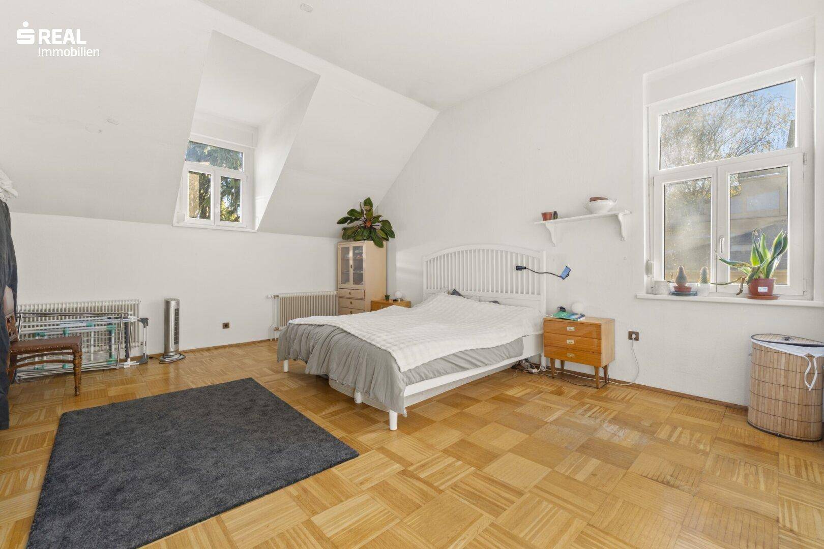 Helles Schlafzimmer im Dachgeschoss mit Dachschrägen, Parkettboden und großen Fenstern.
