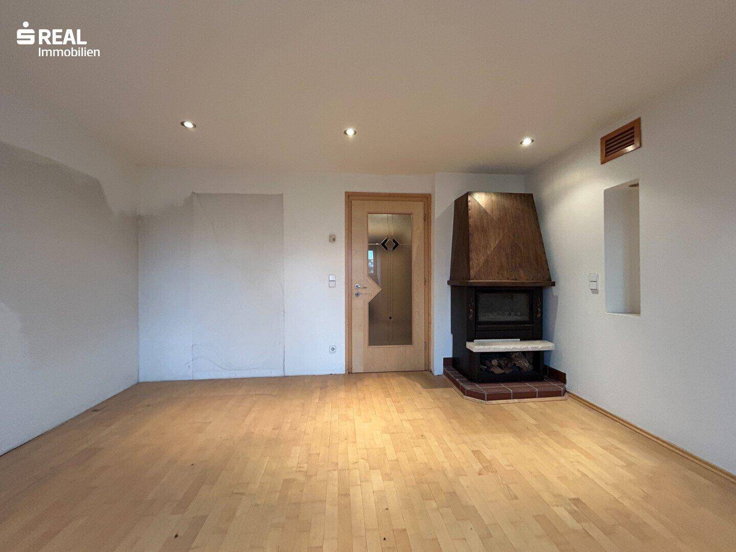 Geräumiges Wohnzimmer mit Holzboden und einem traditionellen Kamin als zentralem Element.