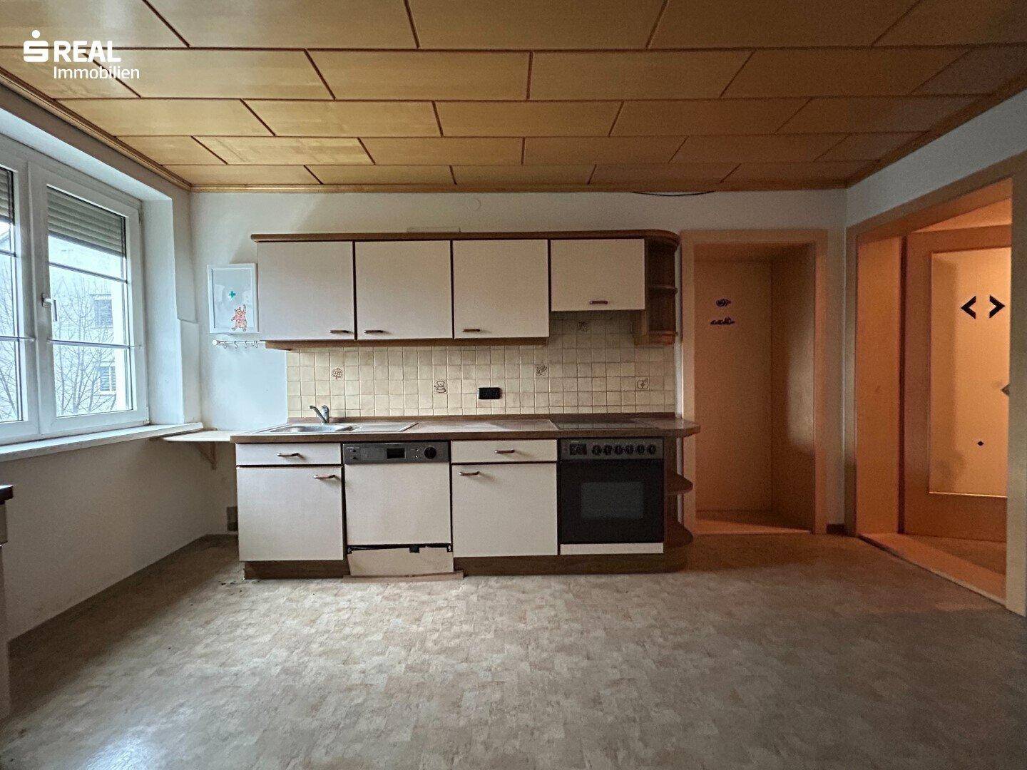 Küche mit älteren Einbauschränken, Spüle, Herd und Holzdeckenverkleidung.