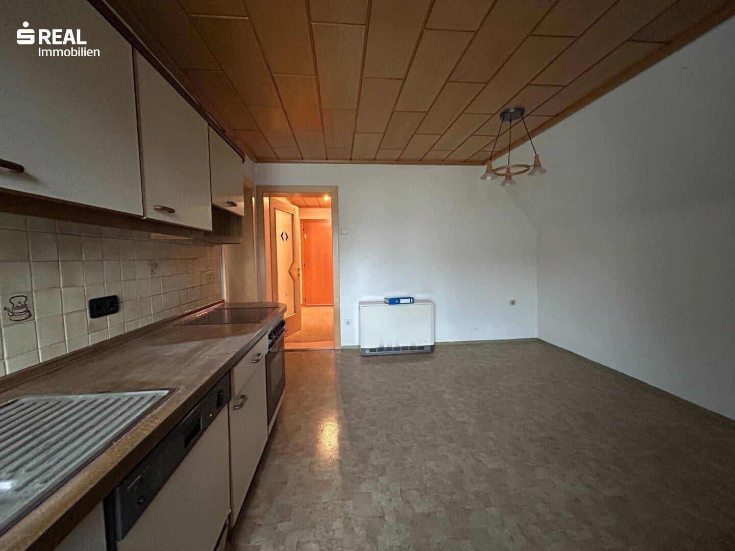 Blick von der Küche in den Flur, mit älteren Küchenmöbeln und Holzdeckenverkleidung.