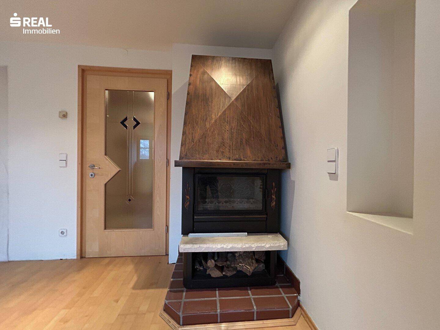 Detailansicht des Kamins mit Holzverkleidung und einer Holztür mit Glaseinsatz.