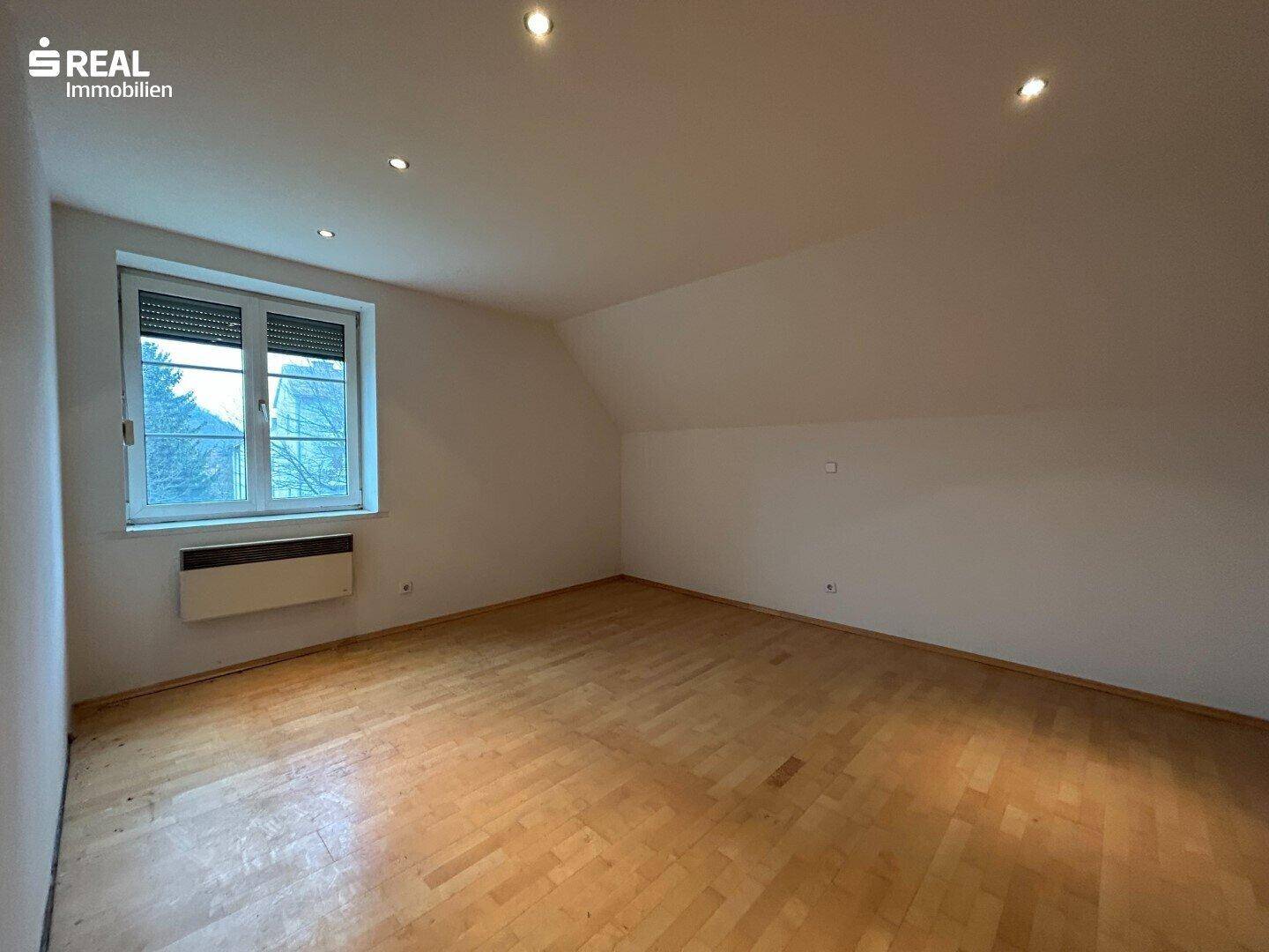 Helles Zimmer mit Holzboden und einem Fenster, das den Blick nach draußen freigibt.