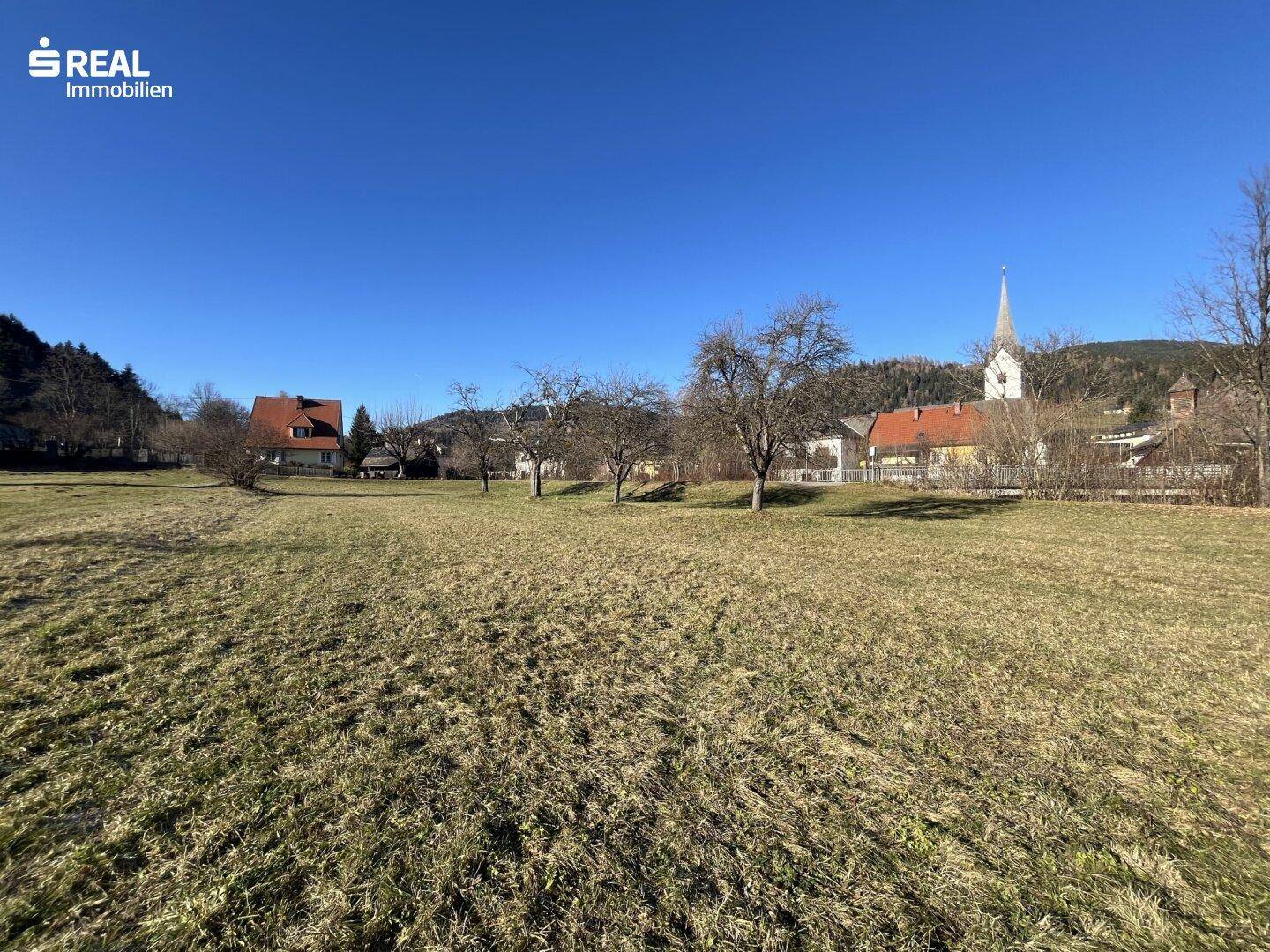 Großes Wiesengrundstück mit Blick auf ein charmantes Dorf und eine Kirche im Hintergrund.