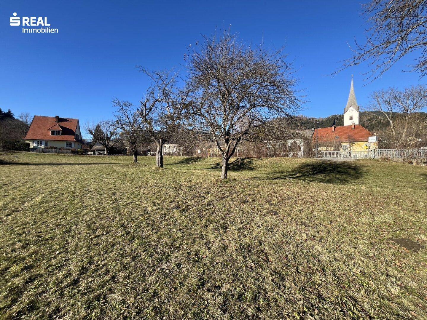 Großes Wiesengrundstück mit Obstbäumen und einem Dorf mit Kirchturm in der ländlichen Umgebung.