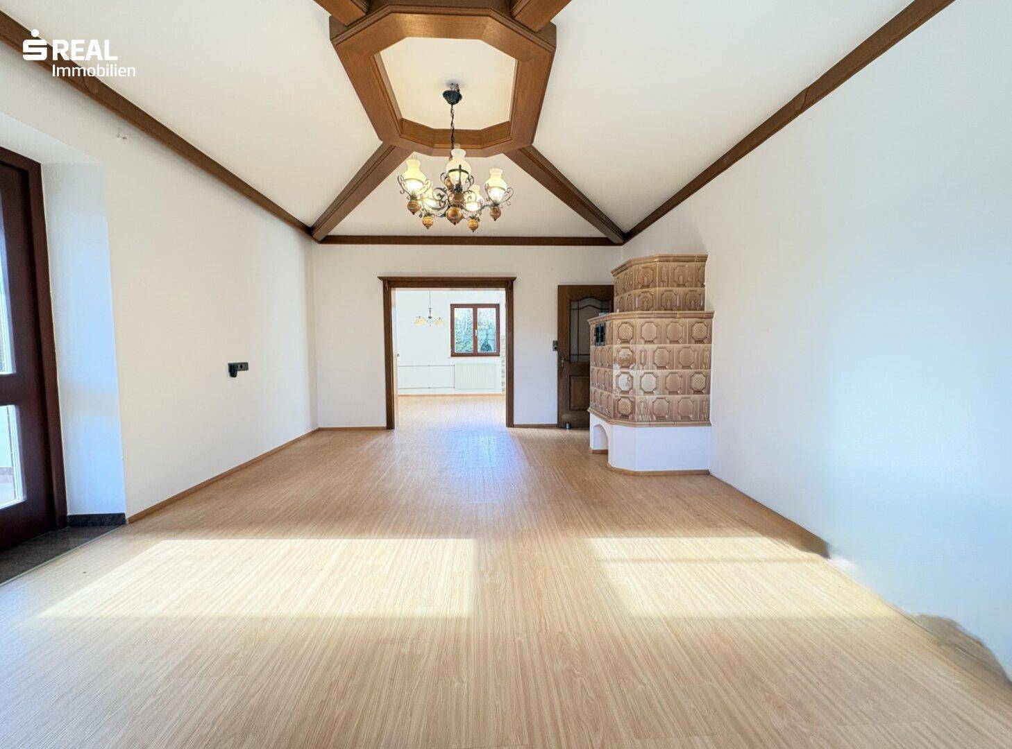 Geräumiges Wohnzimmer mit hellem Laminatboden, Holzbalken und traditionellem Kachelofen.