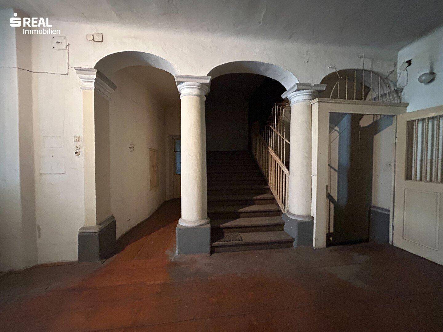Alter Eingangsbereich mit Säulen und gewölbten Durchgängen, die zu einer Treppe in die oberen Stockwerke führen.